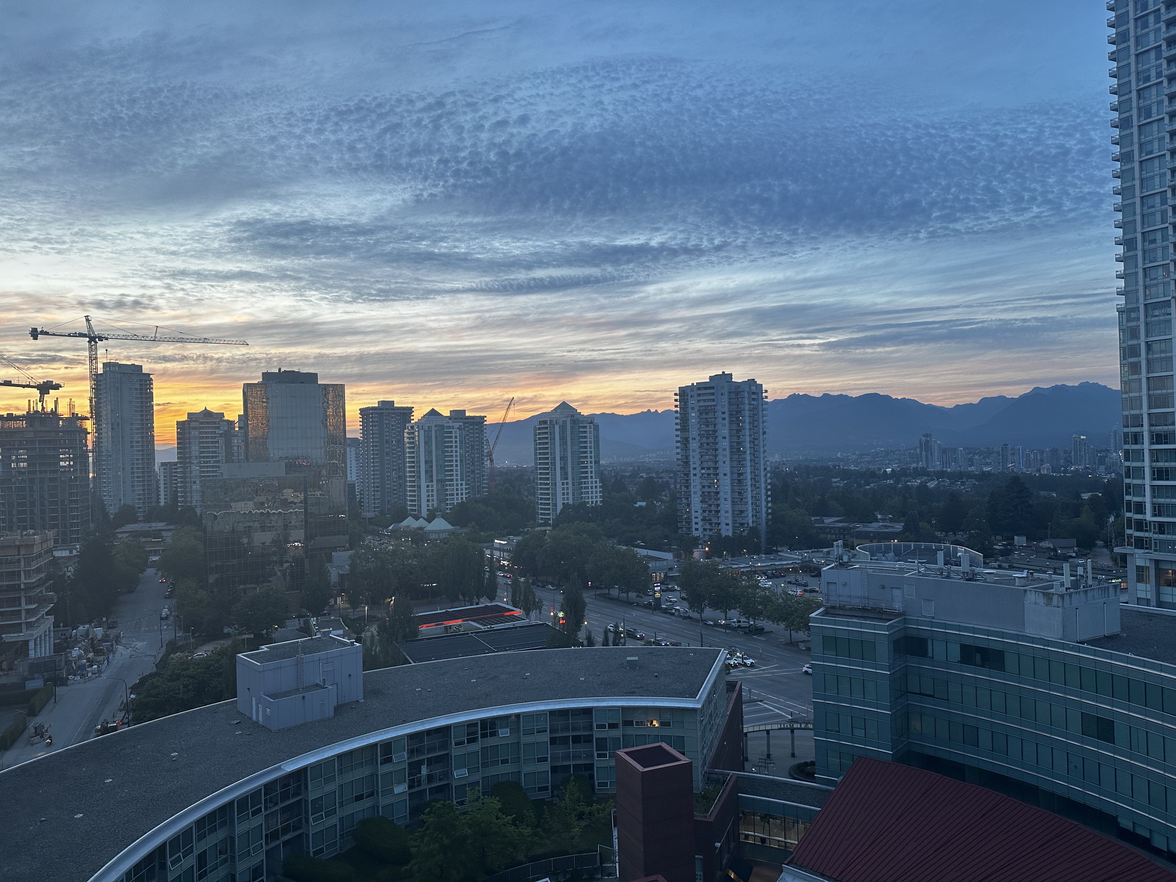 A view from a tall tower of the sunset behind mountains and the Burnaby skyline