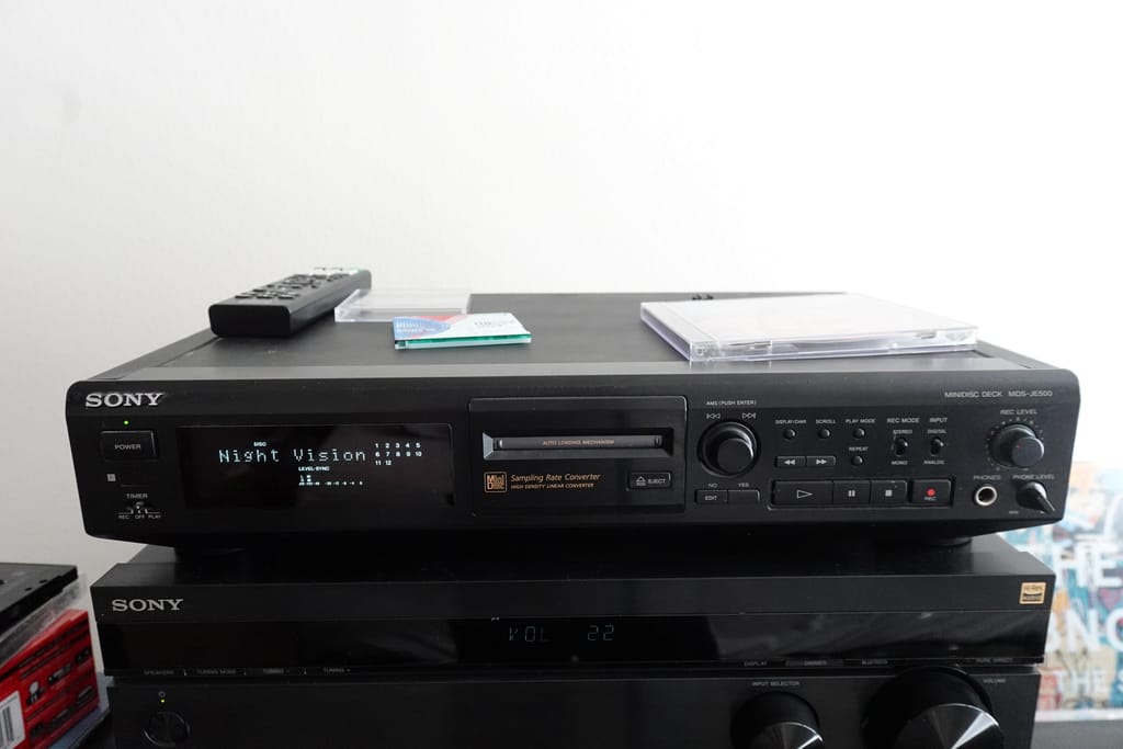 A Sony MDS-JE500 component MiniDisc player sitting at the top of my Hi-Fi stack, with a CD jewel case, MiniDisc, and remote sitting on top