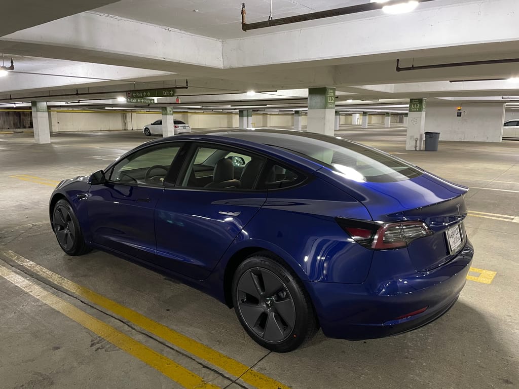 A blue 2021 Tesla Model 3 parked in an empty parking garage