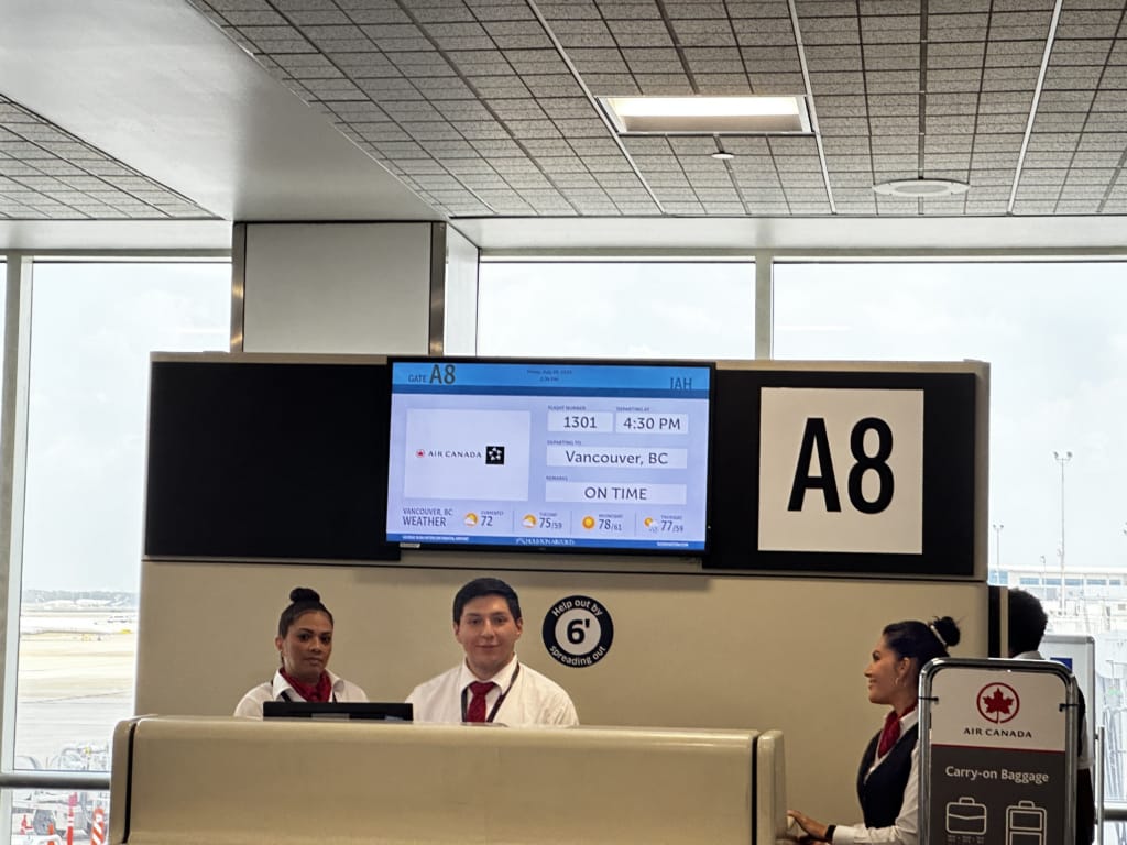 An airport gate with gate agents, showing an Air Canada flight to Vancouver departing next